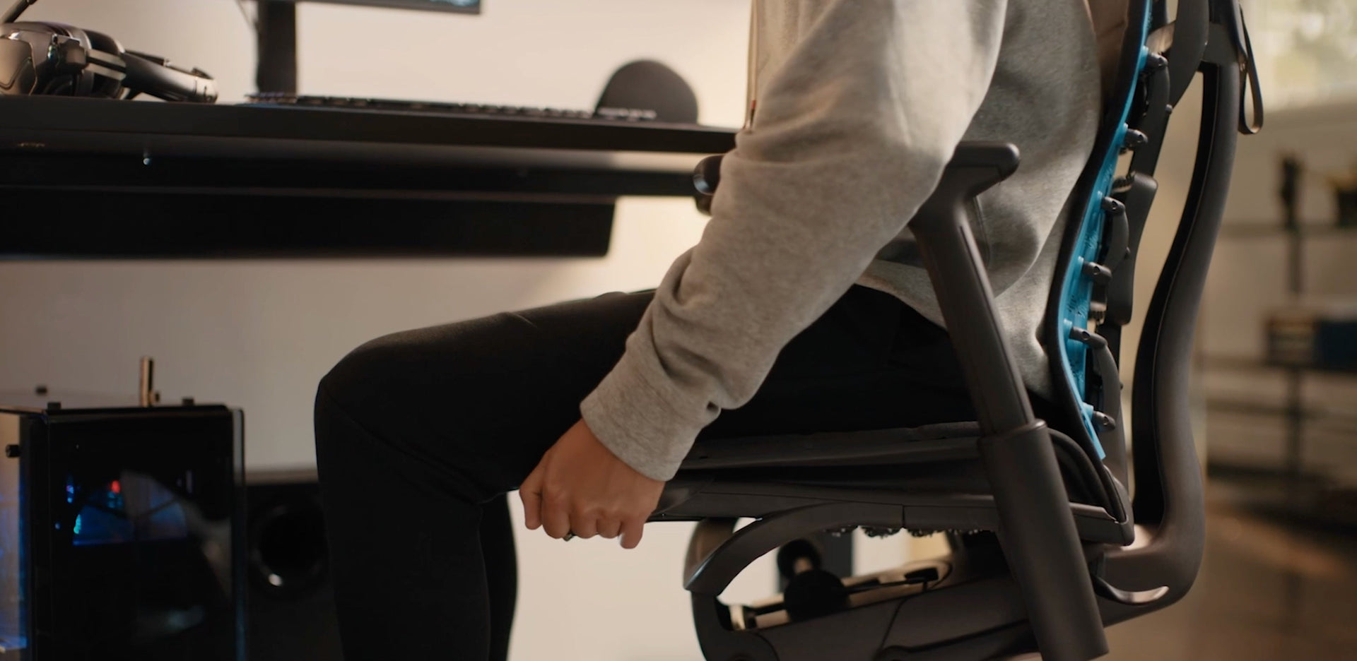 A close-up video of the side of a black Embody Gaming Chair adjustable seat depth mechanism being adjusted by a person in a sweater and trousers.